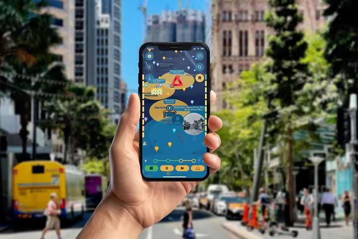 Hand holding a smartphone with Brisbane self-guided dark history walking tour app on a busy city street