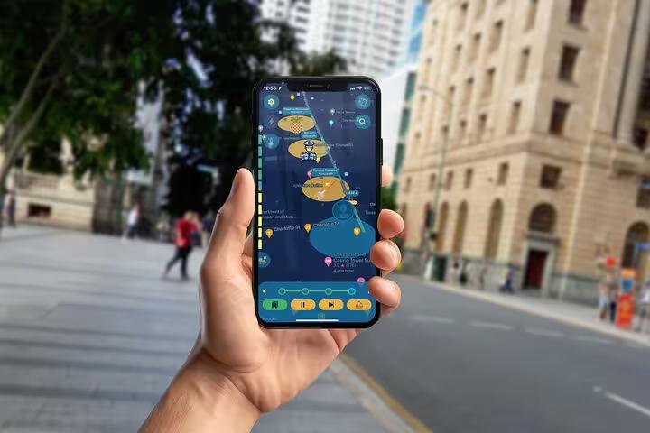 Hand holding a phone displaying Brisbane dark history mystery walking tour map app near historic buildings